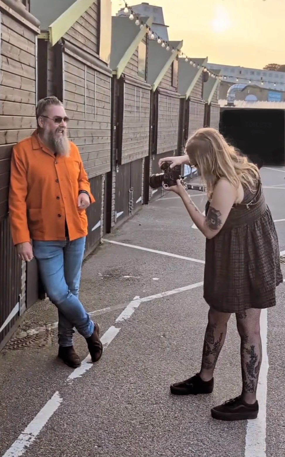 Amy is taking a photo of a man in an orange shirt standing by the hut